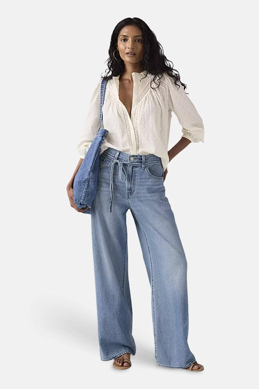 Levi's® middendonkerblauwe spijkerbroek met rechte pijpen, met een strikceintuur en een persoon die een witte blouse draagt.