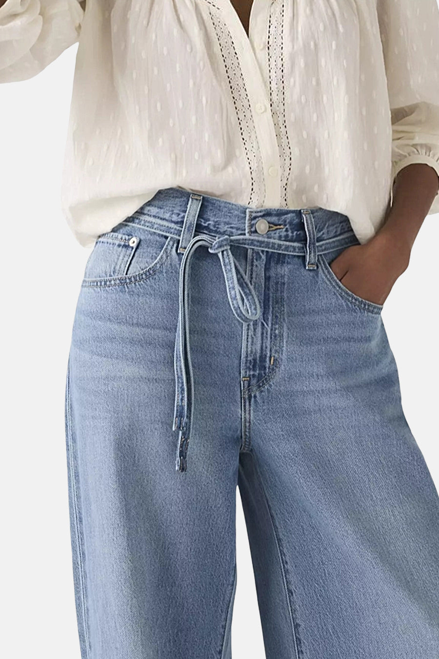 Jean droit en denim bleu moyen de Levi's®, avec une ceinture nouée et une personne portant un chemisier blanc.
