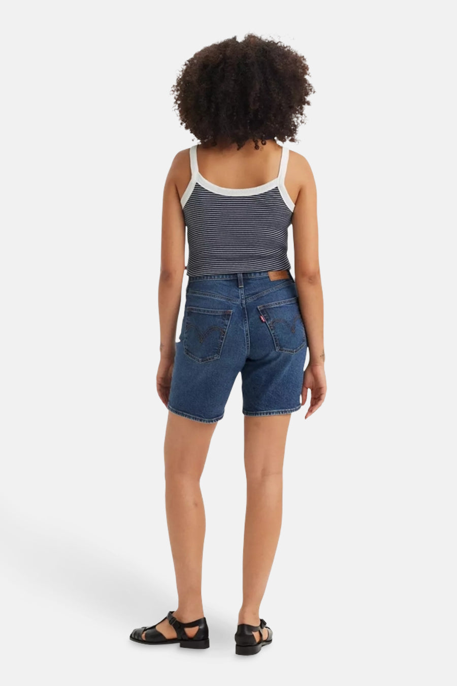 Korte spijkerbroek in blauw van Levi's, achterkant, gedragen met een marineblauwe gestreepte top en zwarte sandalen.
