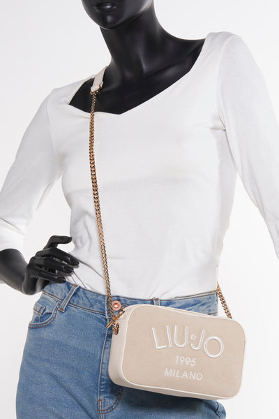 Sac à bandoulière beige de LIU JO avec chaîne dorée, porté avec un jean bleu et un t-shirt blanc.