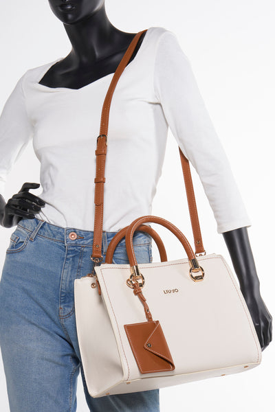 Sac à main écru de LIU JO, avec bandoulière marron, porté par un mannequin en jean et chemise blanche.