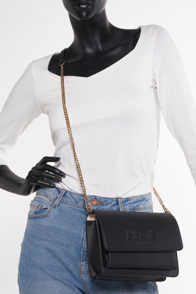 Zwarte schoudertas van LIU JO met een gouden kettingriem gedragen door een model, met een blauwe jeans en een witte top.