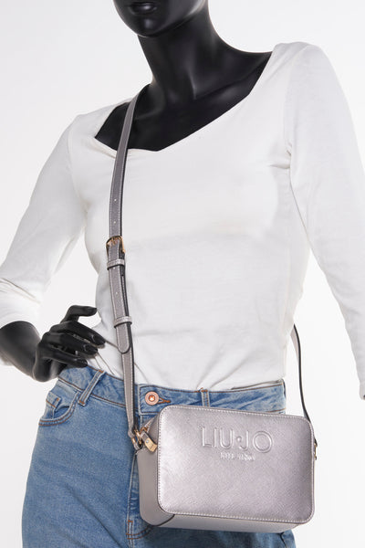 Sac à bandoulière argenté de LIU JO, avec bandoulière réglable, porté avec un jean bleu et un haut blanc.
