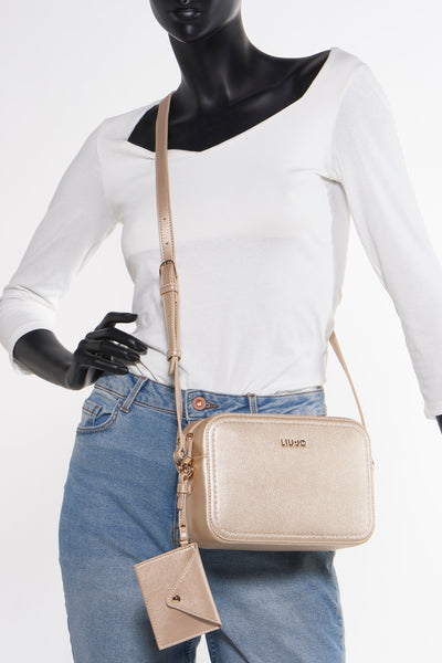 Sac à bandoulière doré de LIU JO, porté avec un jean et un top blanc sur un mannequin noir.
