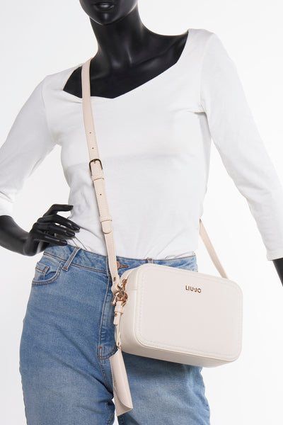 Sac à bandoulière écru de LIU JO, porté sur un mannequin avec un t-shirt blanc et un jean.