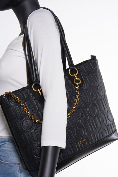 Zwarte Liu Jo handtas met reliëf, met een gouden ketting schouderriem en gedragen door een model.