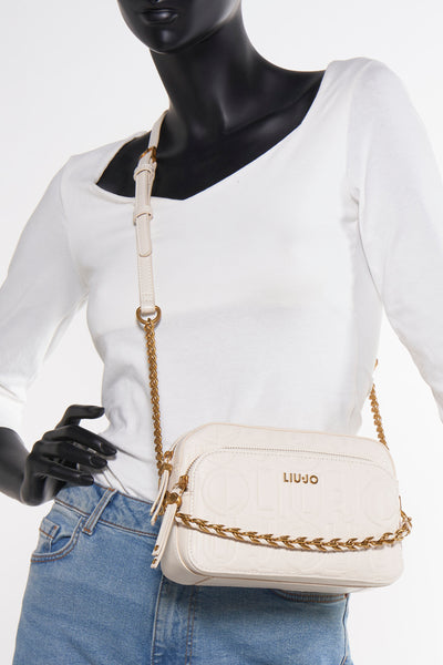 Sac à bandoulière écru de LIU JO avec bandoulière chaîne dorée, porté sur un mannequin en jean et top blanc.
