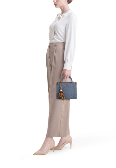 Blauwe handtas van LIU JO, gedragen met een decoratieve bedel, gecombineerd met een witte blouse en een beige broek.