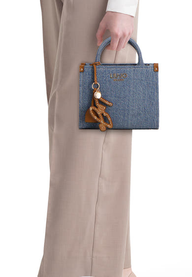 Blauwe spijkerstof handtas van LIU JO, met een bruine decoratieve bedel met opengewerkt patroon, gedragen met een beige broek.