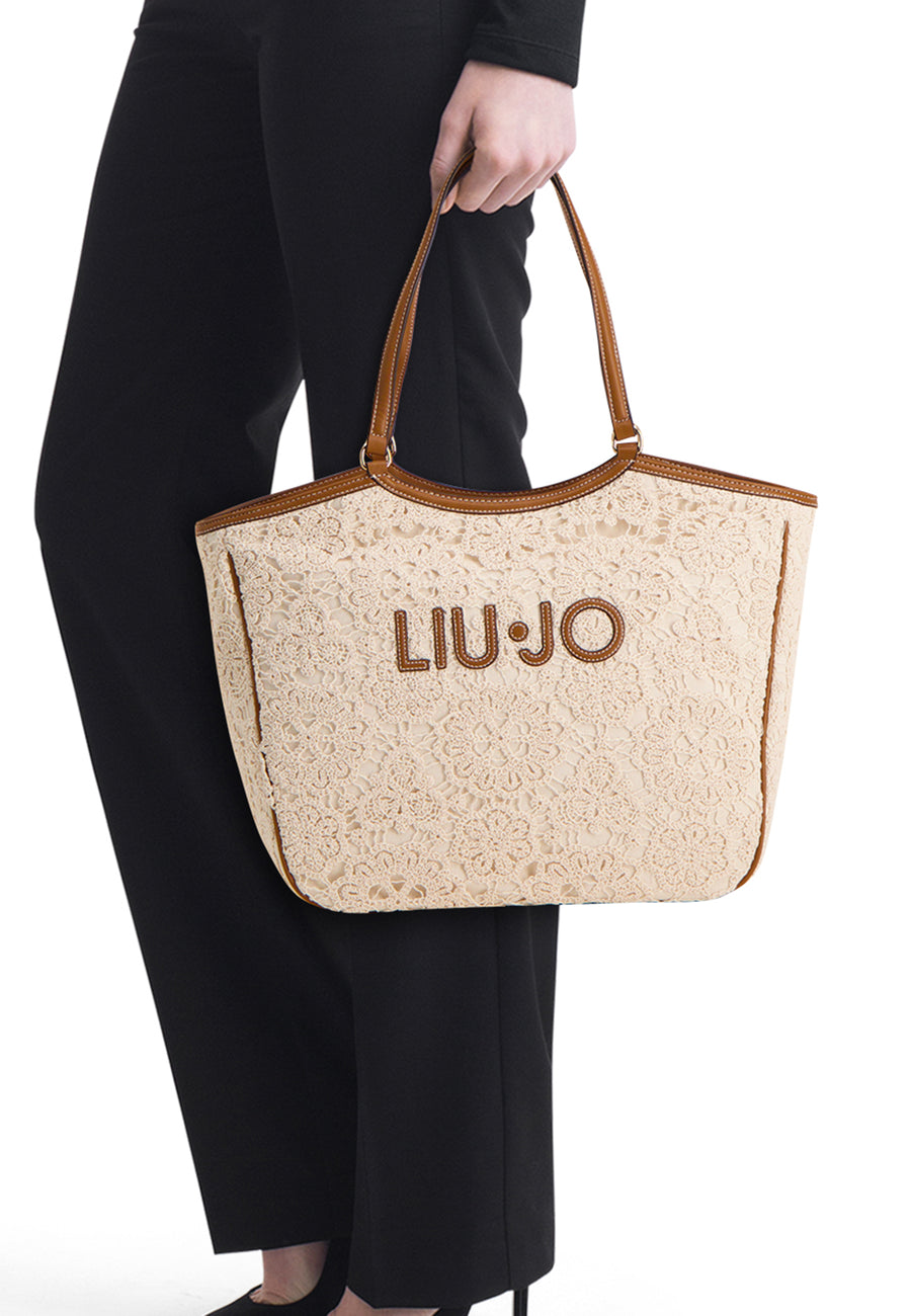 Ecru schoudertas van LIU JO, versierd met bloemenkant, gedragen met een zwarte broek en bijpassende schoenen.
