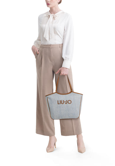 Blauwe schoudertas van LIU JO, met bruine hengsels, gedragen door een model in een beige broek en een witte blouse.