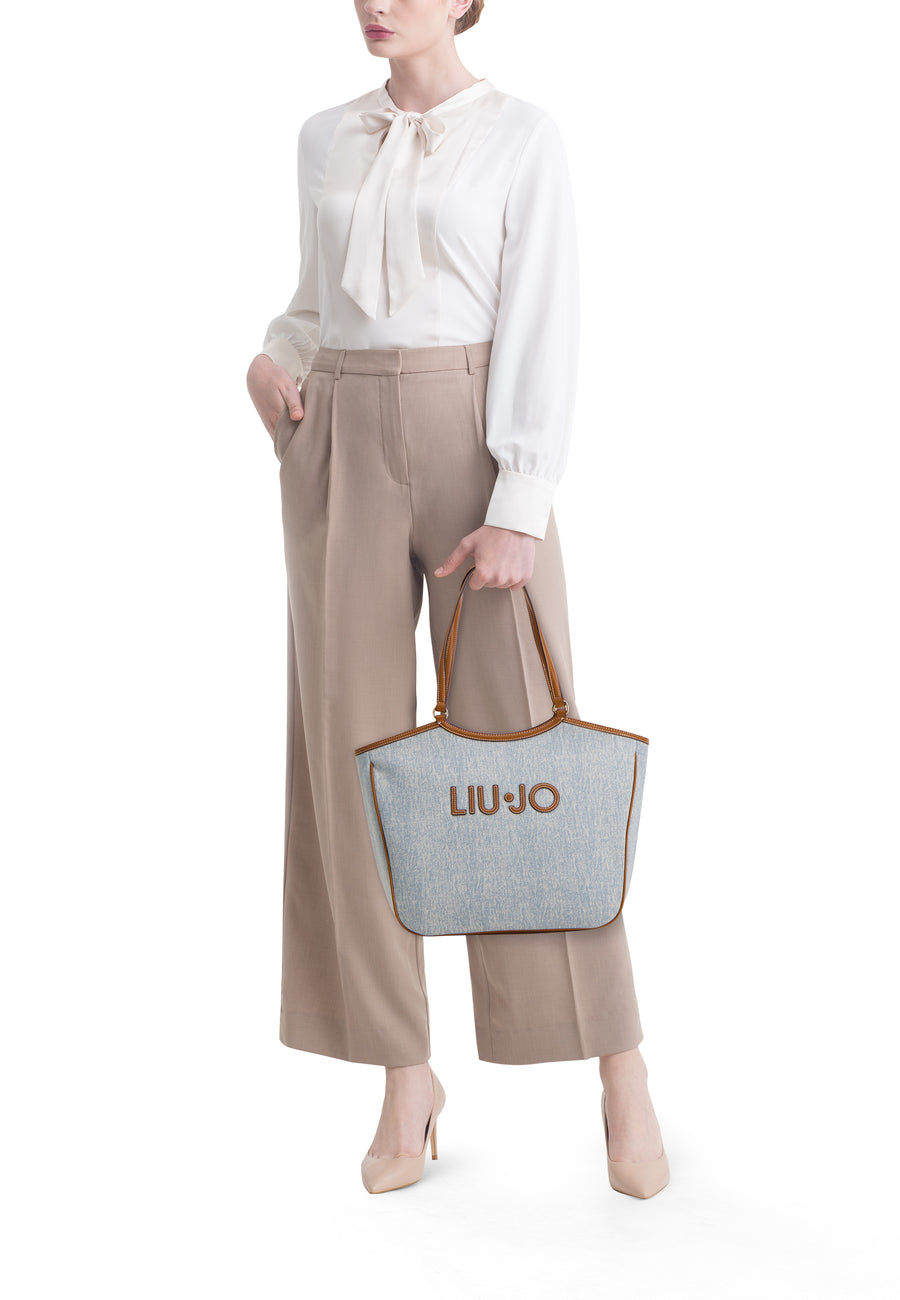 Blauwe schoudertas van LIU JO, met bruine hengsels, gedragen door een model in een beige broek en een witte blouse.