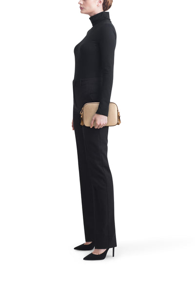 Sac à bandoulière doré de LIU JO, porté avec un pantalon noir et des escarpins noirs à talons hauts.