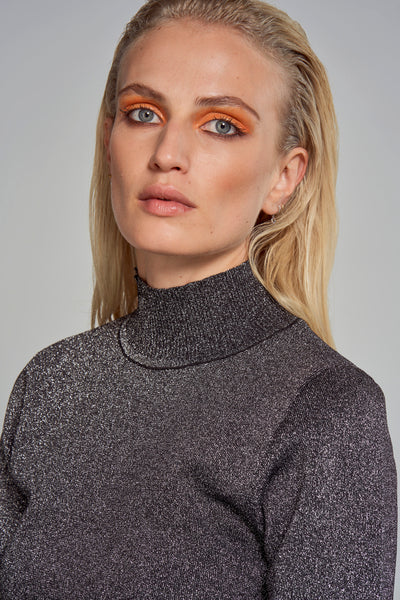 Astrid Black Label zilverkleurige coltrui, in glinsterende gebreide stof, gedragen door een blonde vrouw met blauwe ogen en oranje oogschaduw.