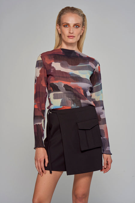 Multicolored long-sleeve blouse with abstract print and sheer pleated texture, worn with black wrap skirt, front view
