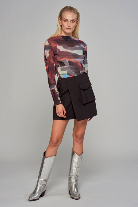 Multicolored long-sleeve blouse with abstract print and ribbed texture, worn with black wrap skirt and silver boots, full-length front view