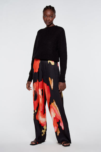 Pull noir de ASTRID Black Label, porté avec un pantalon à motifs floraux et des sandales plates.