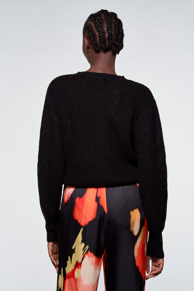 Pull noir en maille d'ASTRID Black Label, porté avec un pantalon à motif floral.
