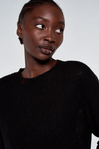 Pull noir à col rond par ASTRID Black Label, en maille texturée sur un mannequin regardant sur le côté.