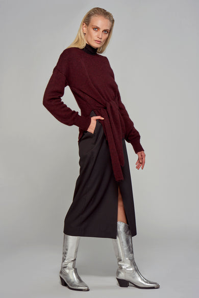 Jupe longue noire ASTRID Black Label, avec une fente, portée avec un pull bordeaux noué et des bottes argentées.

