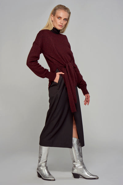 Jupe longue noire ASTRID Black Label, avec une fente, portée avec un pull bordeaux noué et des bottes argentées.
