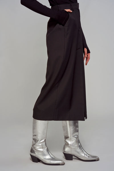 Jupe longue noire par ASTRID Black Label, portée avec des bottes argentées et un haut noir à manches longues.
