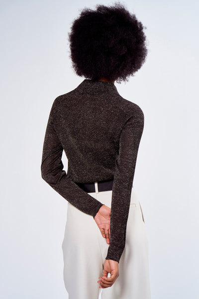 Zwarte polo met lange mouwen van ASTRID Black Label, met glanzende accenten, gedragen met een zwarte riem en een beige broek.