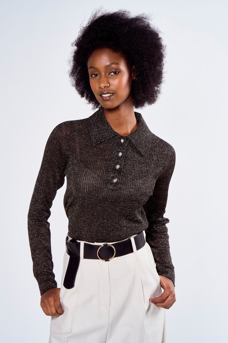 Polo noir scintillant d'Astrid Black Label avec trois boutons, porté avec une ceinture noire et un pantalon taille haute.