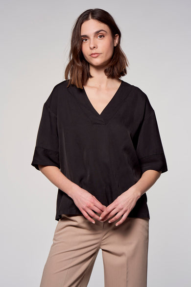 Chemisier à manches courtes noir de ASTRID Black Label, avec encolure en V et pantalon beige.
