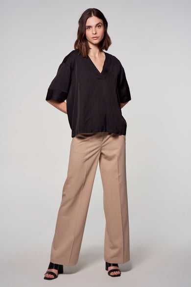 Chemisier noir à manches courtes par ASTRID Black Label, avec un pantalon beige à jambes larges et des sandales.