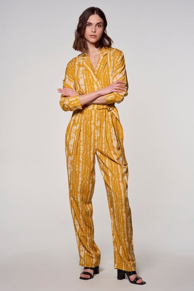 Combinaison jaune à rayures verticales par ASTRID Black Label, avec ceinture à boucle, portée avec des sandales à talons noirs.
