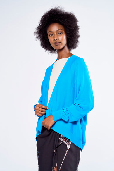 Gilet bleu par Astrid Black Label porté sur un t-shirt blanc et un pantalon noir à motifs.
