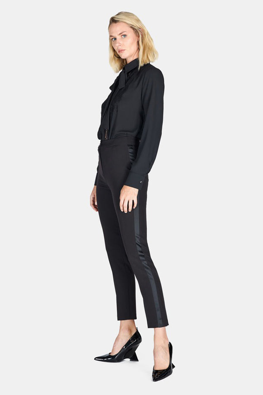 Pantalon coloré noir de ARTIGLI, avec une bande satinée latérale, porté avec un chemisier noir et des escarpins noirs brillants.