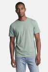 Groen T-shirt met korte mouwen van STROM met een cocktailglas borduursel, gedragen door een man met een lichte spijkerbroek.