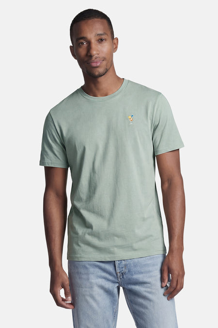 Groen T-shirt met korte mouwen van STROM met een cocktailglas borduursel, gedragen door een man met een lichte spijkerbroek.