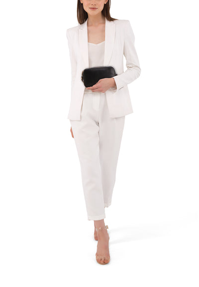 Sac à bandoulière noir de LIU JO, porté avec un tailleur pantalon blanc et des sandales transparentes.
