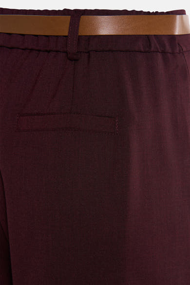 Pantalon de costume rouge bordeaux par AMELIE ET AMELIE, avec ceinture marron et poche passepoilée arrière.
