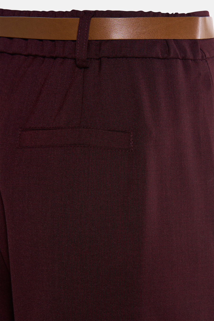 Pantalon de costume rouge bordeaux par AMELIE ET AMELIE, avec ceinture marron et poche passepoilée arrière.
