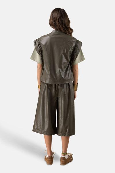 Gilet kaki de ADORE, porté sur un t-shirt vert, avec des bracelets dorés.