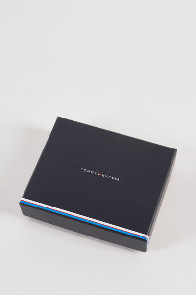 Portefeuille brun de Tommy Jeans, présenté dans sa boîte noire avec rayures bleues, blanches et rouges sur les côtés.
