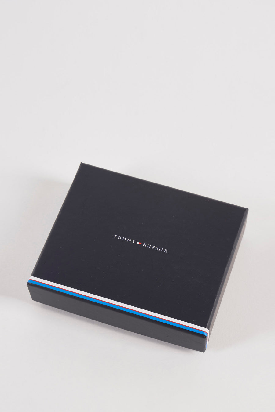 Portefeuille brun de Tommy Jeans, présenté dans sa boîte noire avec rayures bleues, blanches et rouges sur les côtés.
