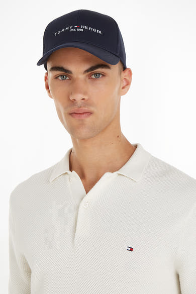 Casquette bleue de TOMMY JEANS, portée par un mannequin en polo texturé blanc cassé