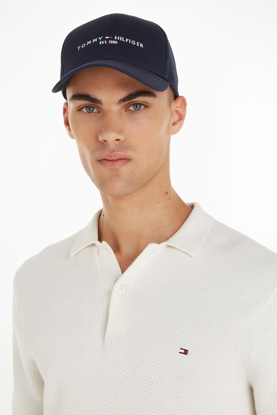 Casquette bleue de TOMMY JEANS, portée par un mannequin en polo texturé blanc cassé