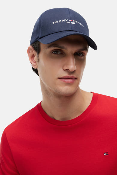 Casquette bleue de TOMMY JEANS, portée par un homme en t-shirt rouge uni avec logo sur la poitrine.