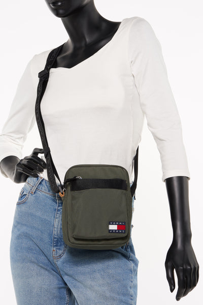 Groene schoudertas van TOMMY JEANS gedragen door een model met een spijkerbroek en een wit topje.