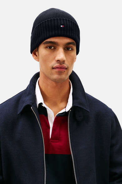 Tommy Jeans blauwe muts, in ribgebreide stof met vlaglogo, gedragen met gestreept poloshirt en marineblauwe gewatteerde jas.