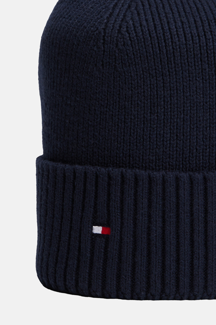 Gros plan sur un bonnet bleu marine TOMMY JEANS en maille côtelée avec revers et petit drapeau brodé.