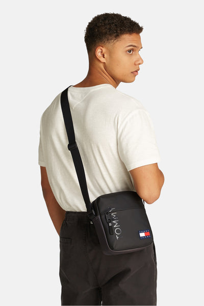 Zwarte schoudertas van Tommy Jeans, gedragen met een wit T-shirt en een donkere broek.