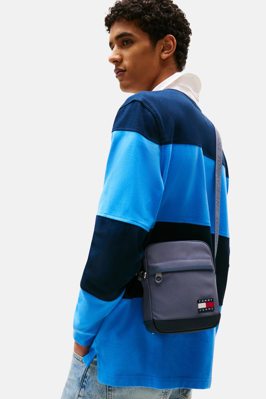 Sac à bandoulière bleu de Tommy Jeans, porté avec une bandoulière logotypée et un polo à rayures.
