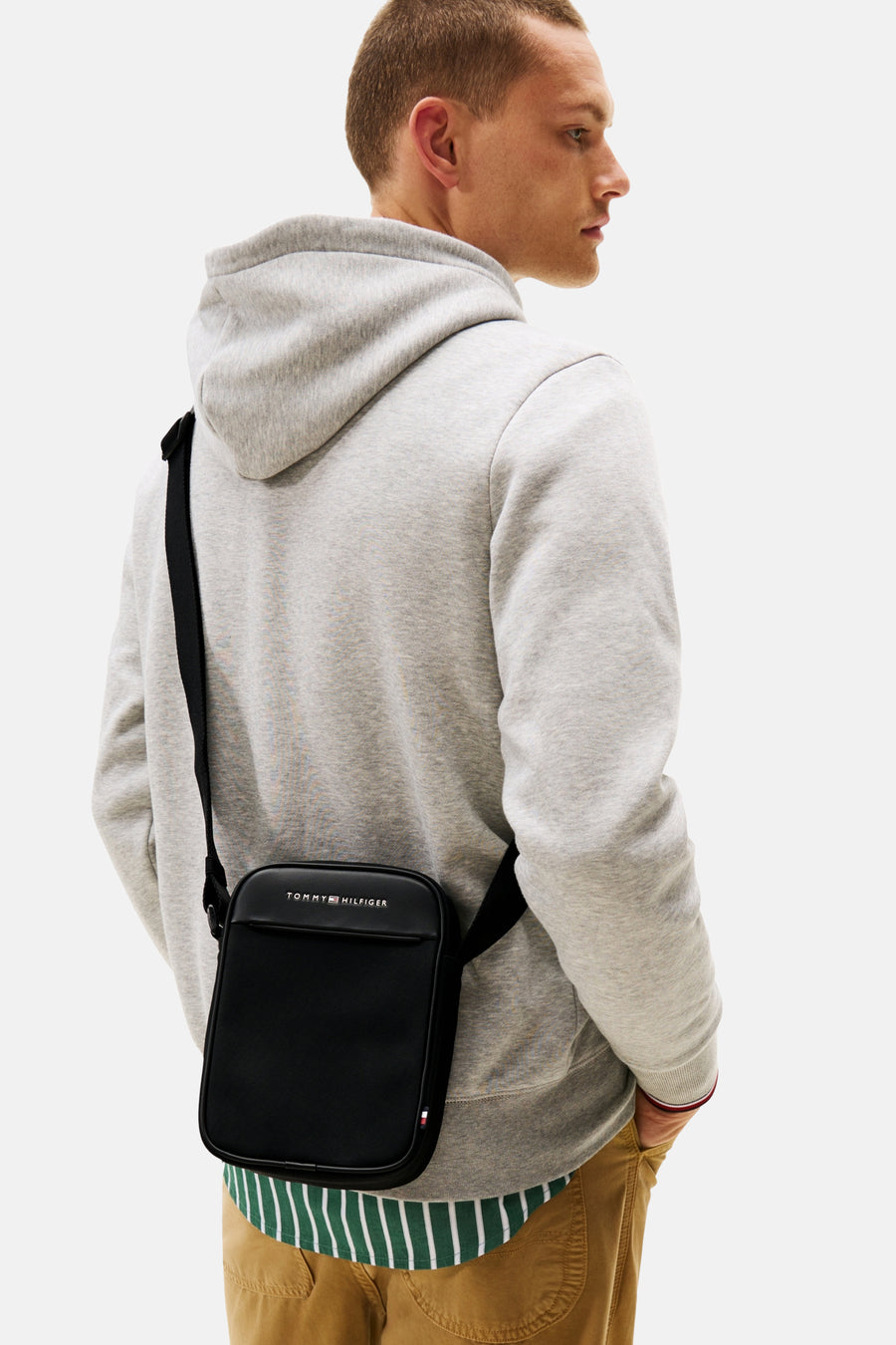 Zwarte schoudertas van TOMMY JEANS met zwarte schouderriem gedragen door een man in een grijze hoodie.